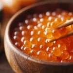 fresh salmon eggs (ikura) in a wooden bowl, with chopsticks lifting a few pearls